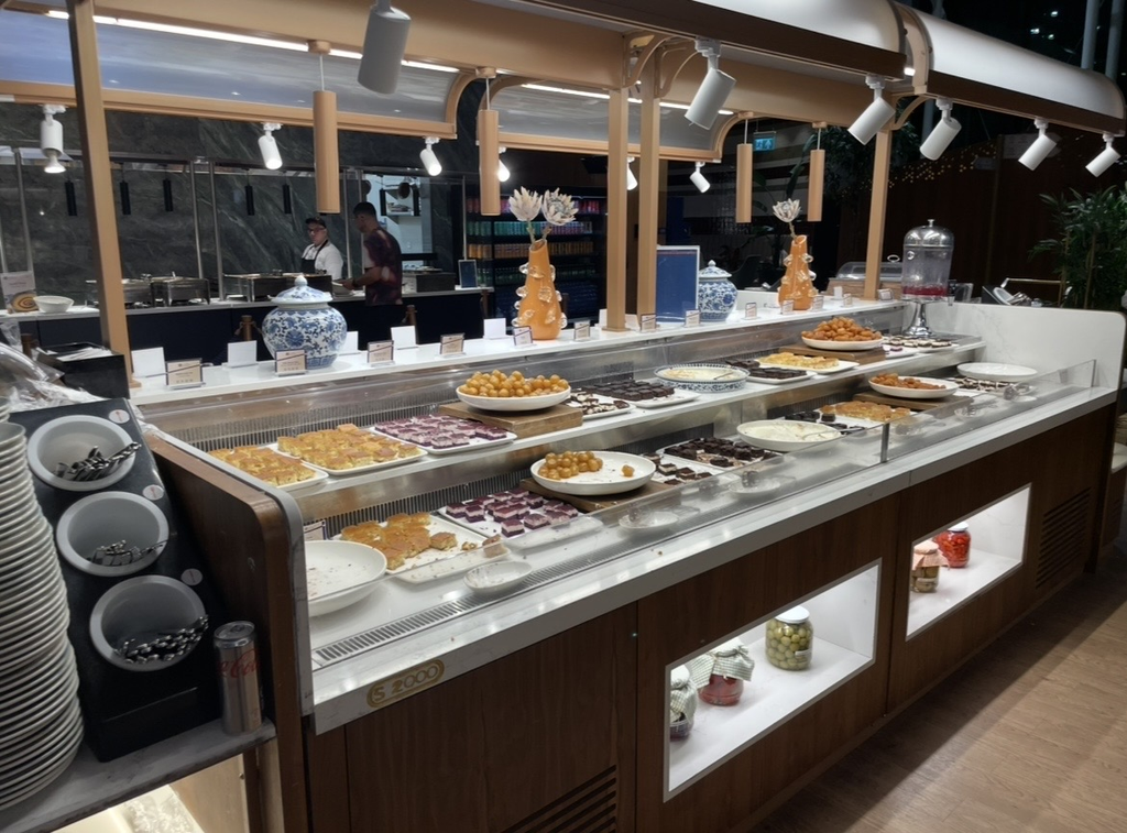 IGA 貴賓室的自助餐檯，甜點區陳列蛋糕、酥點與油炸甜食，搭配裝飾陶器與燈光營造華麗氛圍。