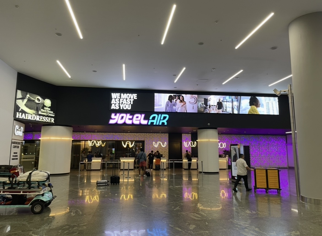 伊斯坦堡國際機場內的 YOTELAIR 入口，旅客在紫色發光標誌與未來感燈光、數位指示牌前的接待區辦理入住。