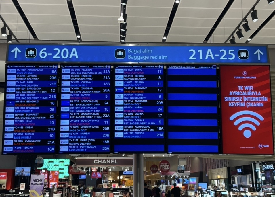 伊斯坦堡國際機場抵達區的行李提領資訊看板，顯示各航班的抵達狀況與行李轉盤編號，下方可見品牌店舖，呈現熱鬧的抵達大廳景象。