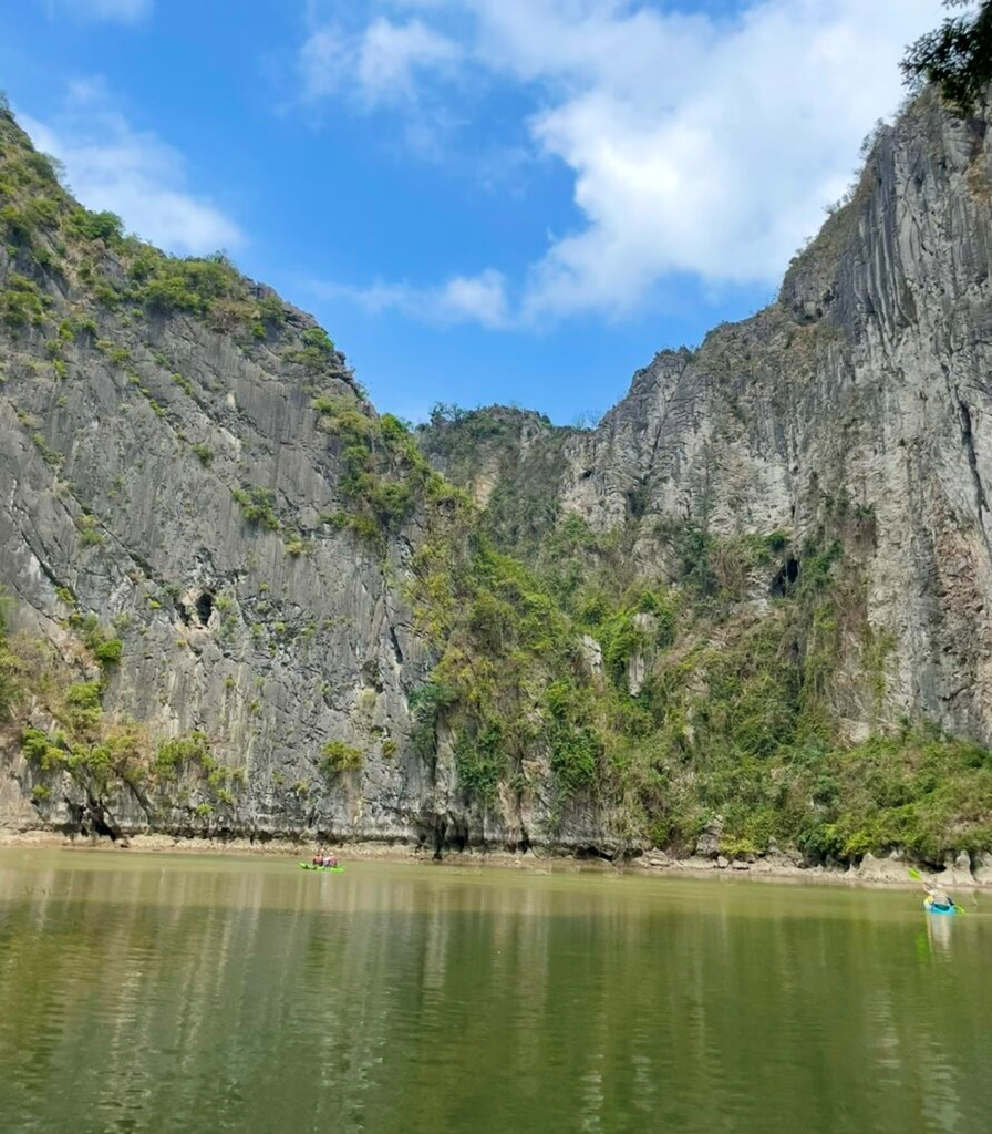 遊船在下龍灣平靜的水面上緩緩前行，四周被石灰岩峭壁環繞，呈現被奇岩包覆的寧靜景觀。
