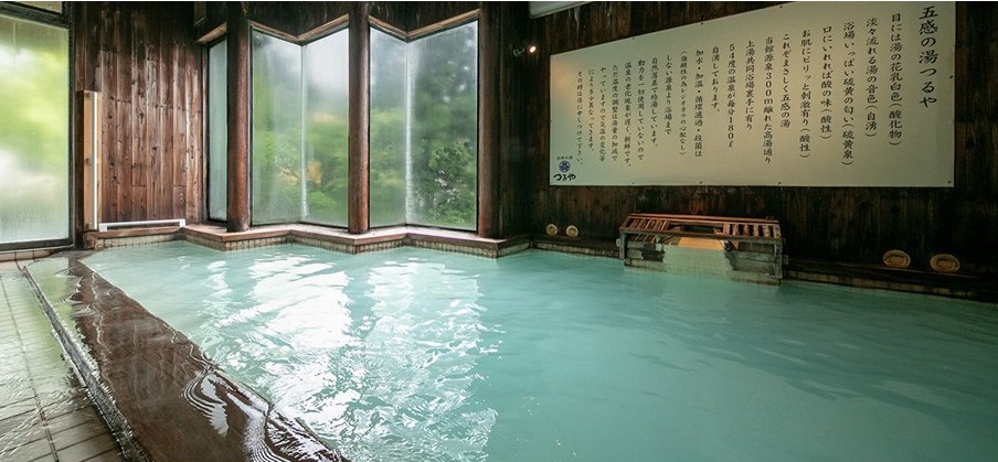 五感の湯つるやの大浴場。木の温もりある内装に乳白色の湯が満ち、湯口から源泉が流れ込む静かな温泉空間で、蔵王温泉の強酸性泉らしい雰囲気が伝わる。