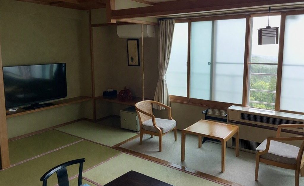 五感の湯つるやの和室客室。畳敷きの部屋に低い木製テーブルと椅子が置かれ、障子越しに緑が見える落ち着いた空間で、蔵王温泉らしい和の雰囲気が感じられる。