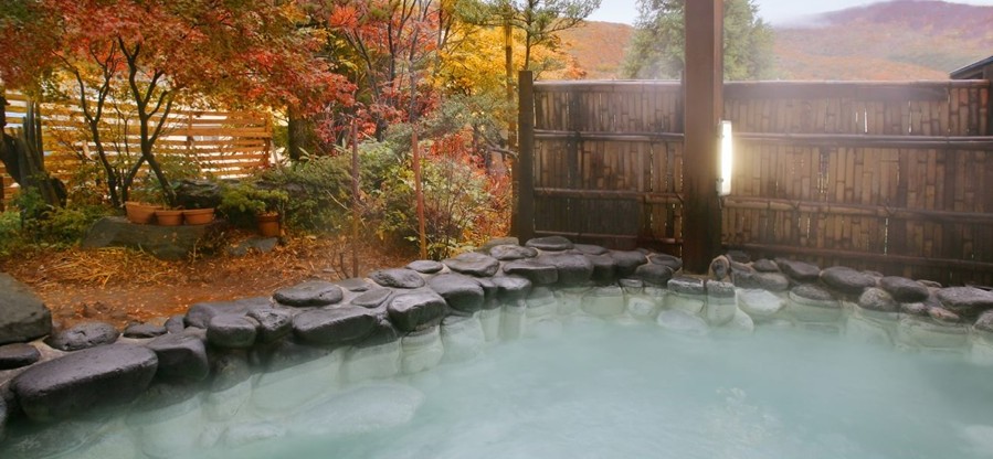 五感の湯つるやの露天風呂。紅葉に囲まれた石造りの湯船から湯けむりが立ち上り、自然の景色を楽しみながら入浴できる蔵王温泉らしい開放的な温泉。