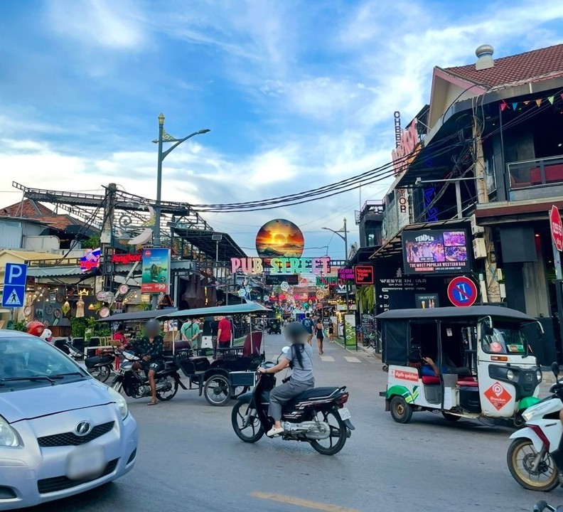 柬埔寨暹粒酒吧街（Pub Street）的入口街景，嘟嘟車與機車在標誌性招牌旁通行。