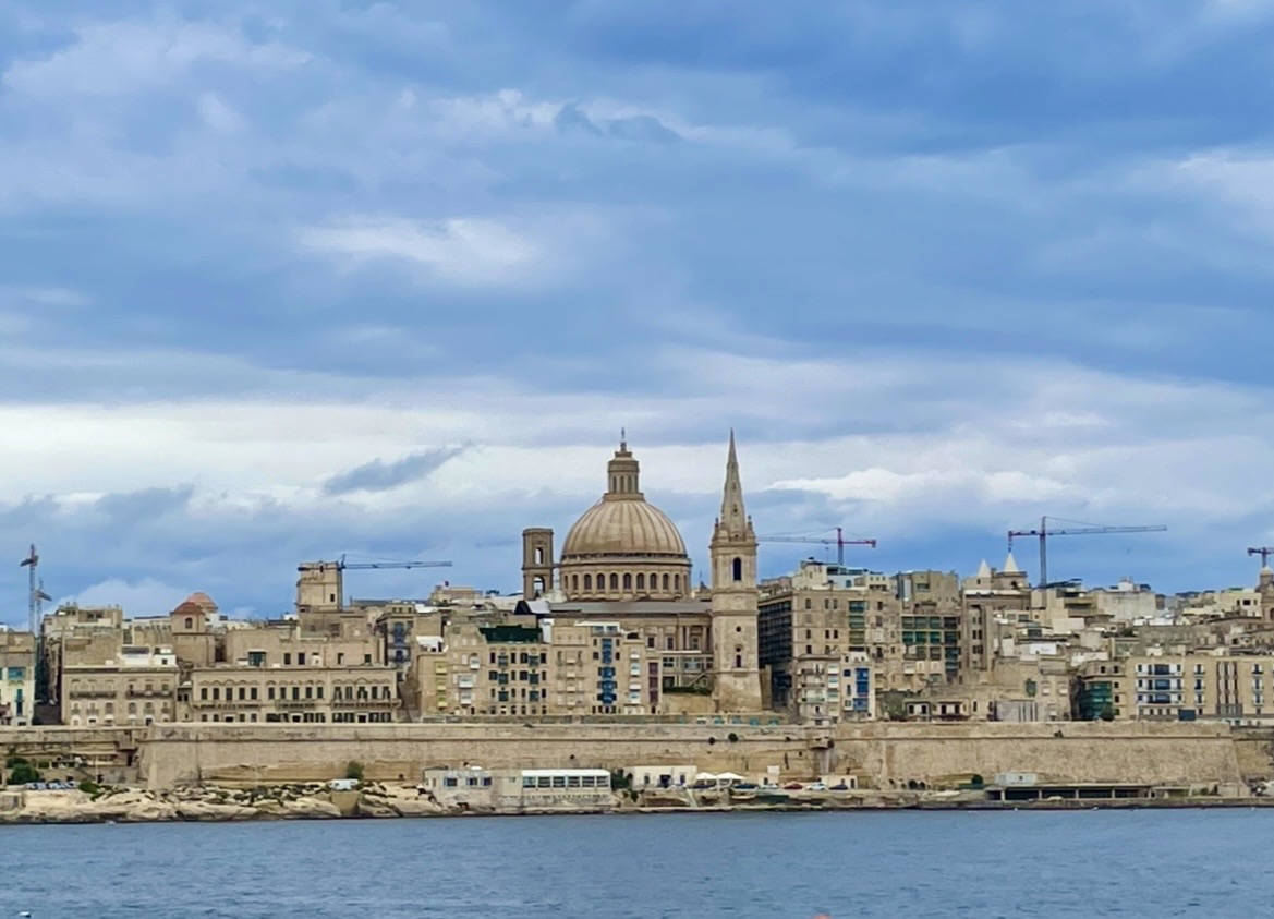 Valletta’s iconic waterfront skyline, with stone buildings and a prominent dome rising above the coast, showcasing the historic city’s striking beauty.