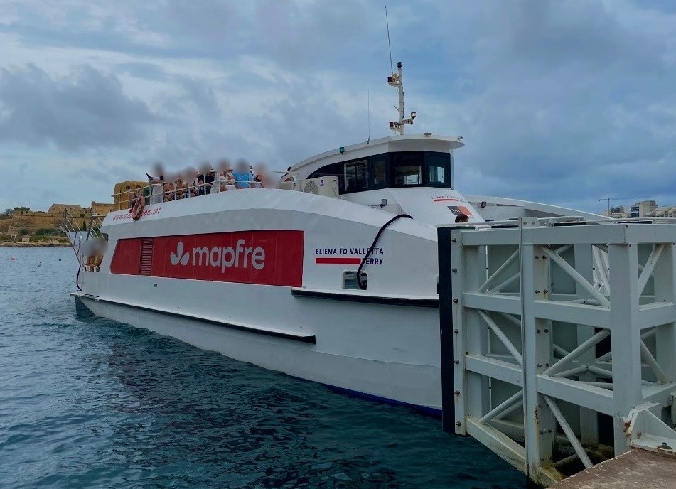 マルタの海に浮かぶ、2階のデッキ席に多くの乗客が乗った「SLIEMA TO VALLETTA FERRY」の白と赤のフェリー。