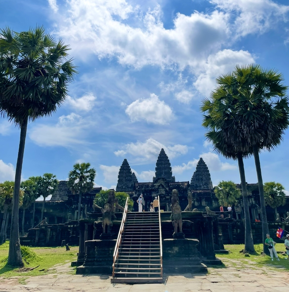 吳哥窟（Angkor Wat）的正門石階，高聳棕櫚樹與晴空環繞的主體建築入口。