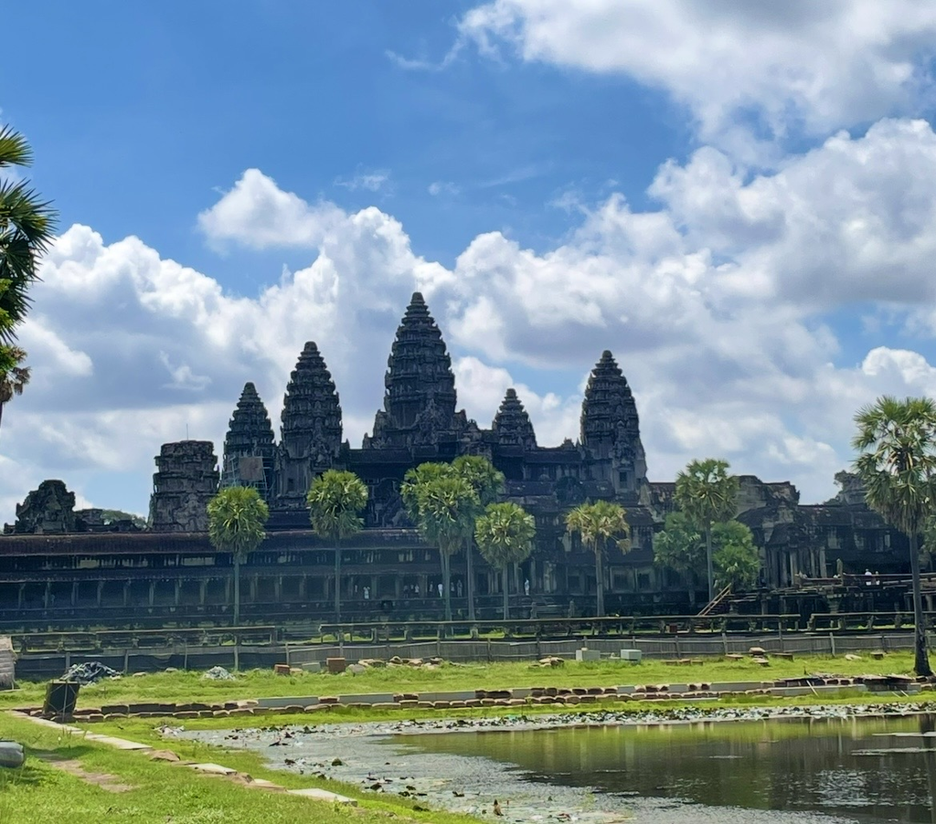 從聖池畔遠眺吳哥窟（Angkor Wat）的神廟全景，倒映水面與晴空下的中央高塔。