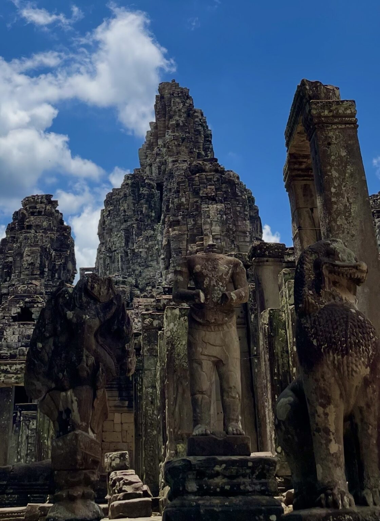 巴戎寺（Bayon Temple）內矗立的無頭石像與守護石獅，背景為高聳的石造神塔。