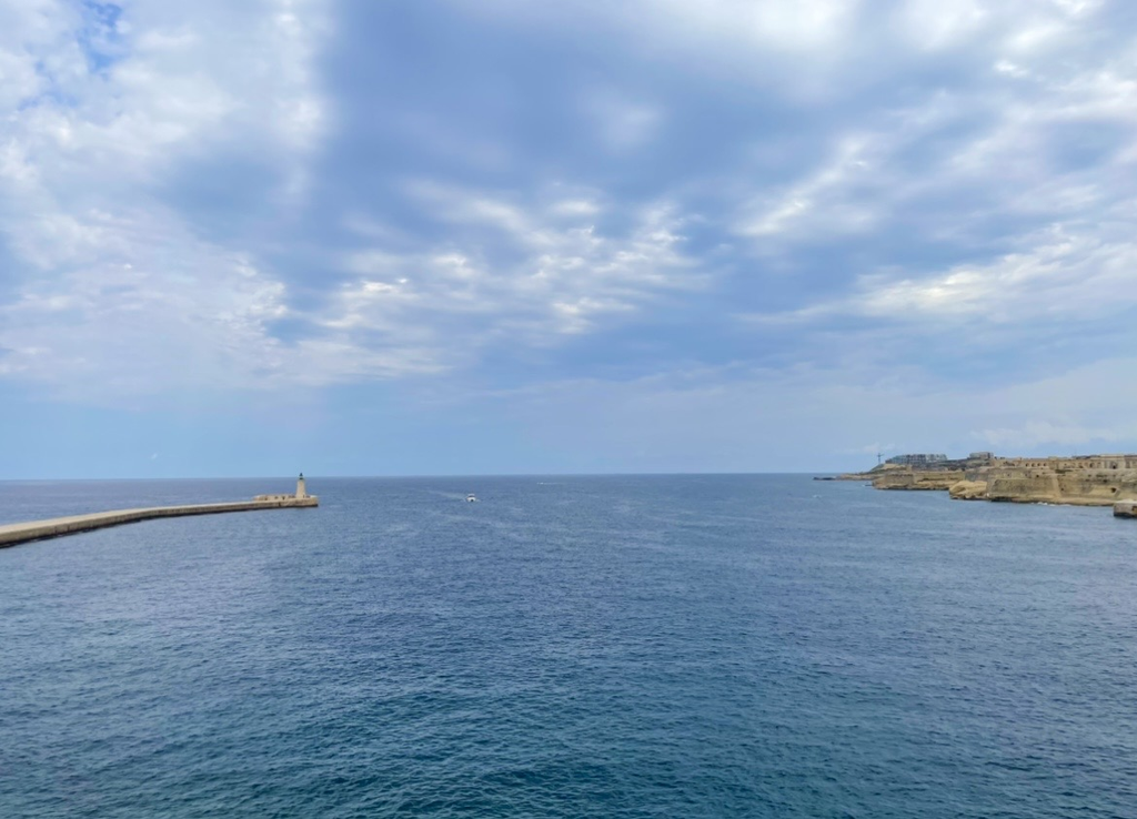 從聖埃爾莫堡眺望地中海，防波堤與燈塔延伸在平靜的海面上，岸邊的要塞遺構與海景交織出寧靜的風光。