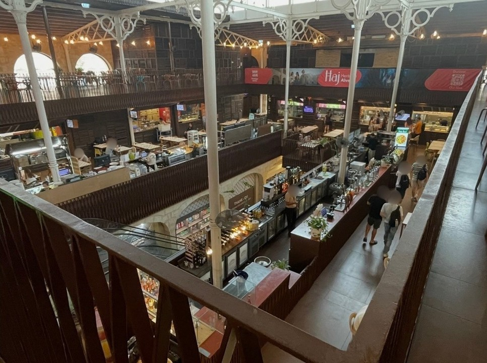 瓦勒他美食市集 Is‑Suq tal‑Belt 的室內空間，白色鐵柱與天窗照亮歷史建築，形成結合古蹟與現代美食區的熱鬧場景。