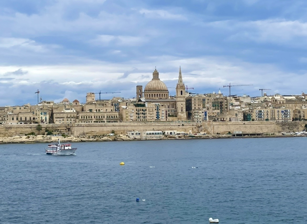 A view of Valletta from Sliema, with the large dome and slender spires rising above dense historic buildings across the water, creating a striking and picturesque cityscape.