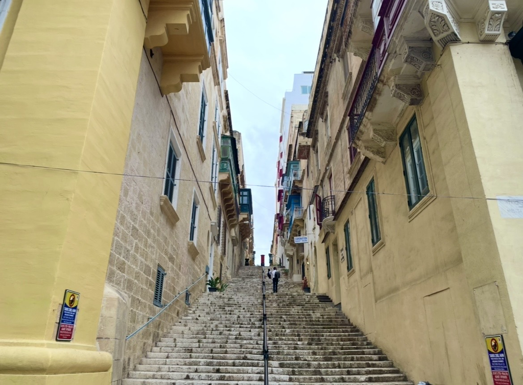 Steep stone steps winding through Valletta’s old town, lined with stone buildings and colorful wooden balconies. A historic Maltese streetscape full of character and charm.